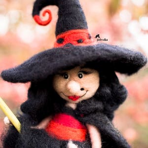 May include: A felt witch doll with a black hat, red and black dress, and a black broom. The doll has a smiling face with red lips and a black nose.
