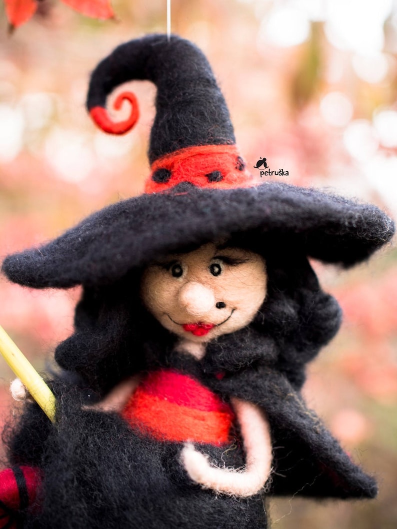 May include: A felt witch doll with a black hat, red and black dress, and a black broom. The doll has a smiling face with red lips and a black nose.