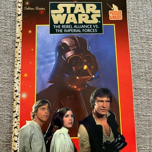 Pode incluir: Um livro vintage de Star Wars da Golden Books com Darth Vader, Luke Skywalker, Princesa Leia e Han Solo na capa. O título é "The Rebel Alliance vs. The Imperial Forces" com quebra-cabeças e labirintos.