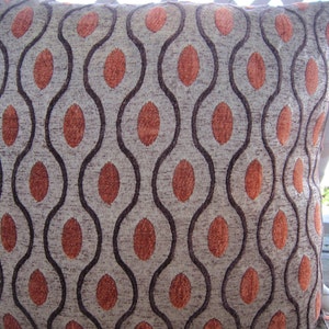 May include: A decorative throw pillow with a brown and orange geometric pattern. The pillow has a wavy design with orange circles on a beige background.