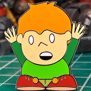 Könnte beinhalten: Ein Cartoon-Emaille-Pin mit einer Figur mit orangefarbenem Haar, einem grünen Hemd, roten Schuhen und hoch erhobenen Armen in einer überraschten Geste. Der Pin hat eine schwarze Umrandung und befindet sich vor einem grünen Gitterhintergrund.