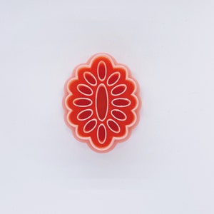 Op de afbeelding: Een roze en rode plastic koekjesvormer in de vorm van een bloem met een centrale ovale vorm.