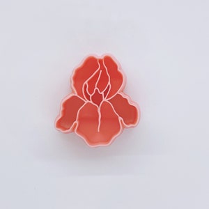 May include: A pink plastic cookie cutter shaped like an iris flower.