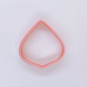May include: A light pink petal-shaped cookie cutter. The cutter is made of plastic and has a smooth, rounded edge. The cutter is designed for creating flower-shaped cookies or other baked goods.