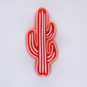 May include: A pink and red cactus shaped cookie cutter. The cutter is made of plastic and has a detailed design.