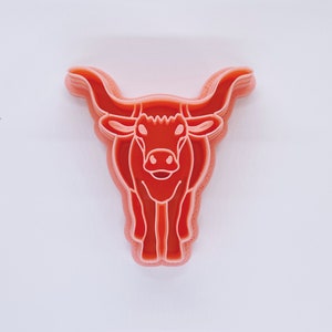 May include: A pink plastic cookie cutter shaped like a bull's head with large horns.