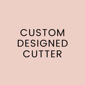 May include: The words "CUSTOM DESIGNED CUTTER" are displayed in a bold, black font against a soft, blush-colored background. The text is centered and stacked vertically, creating a clean and modern design.