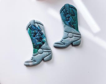 Puede incluir: Dos pendientes de arcilla polimérica en forma de bota vaquera azul y verde con detalles de purpurina.