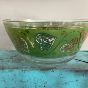 Op de afbeelding: Een glazen kom met een groen en gouden ontwerp. De kom heeft een patroon van bladeren en swirls.