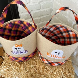 May include: Two burlap trick-or-treat bags with orange and black plaid fabric. One bag has a ghost with the name "Sophia" embroidered on it. The other bag has a ghost with the name "William" embroidered on it.