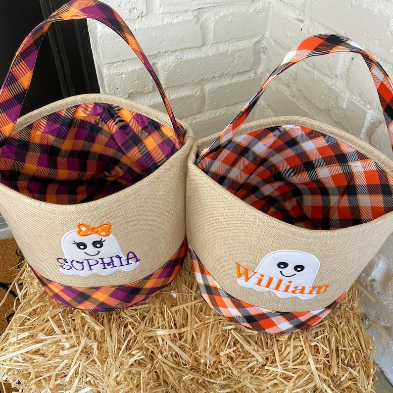 May include: Two burlap trick-or-treat bags with orange and black plaid fabric. One bag has a ghost with the name "Sophia" embroidered on it. The other bag has a ghost with the name "William" embroidered on it.