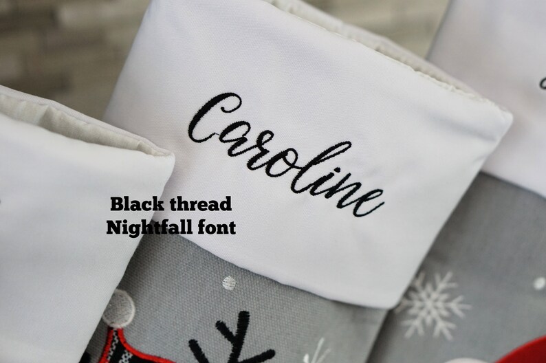 May include: A gray Christmas stocking with a white cuff featuring the name Caroline embroidered in black thread using Nightfall font. The stocking is decorated with embroidered snowflakes and a partial graphic design.