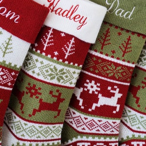May include: A set of four knitted Christmas stockings featuring red, green, and white geometric patterns, including reindeer and pine tree motifs. Each stocking has a solid-colored cuff embroidered with names such as Mom, Hadley, and Dad.