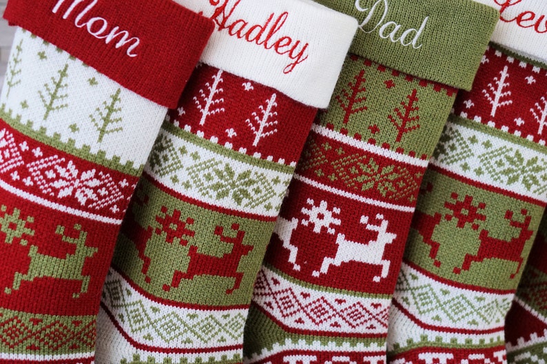 May include: A set of four knitted Christmas stockings featuring red, green, and white geometric patterns, including reindeer and pine tree motifs. Each stocking has a solid-colored cuff embroidered with names such as Mom, Hadley, and Dad.