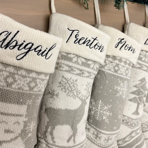 May include: Set of six gray and white knit stockings with personalized names: Abigail, Trenton, Mom, Dad, Ben, and Grandma. The stockings feature a snowflake and reindeer design.