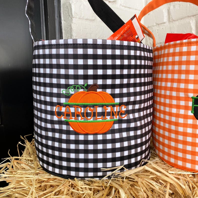May include: Black and white checkered fabric trick-or-treat bucket with a green stem orange pumpkin and the name "CAROLINE" embroidered on it.