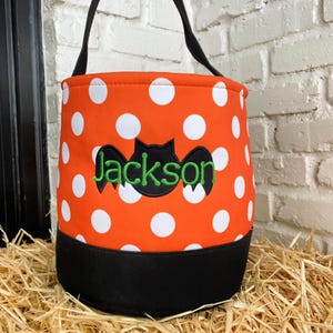 K&ouml;nnte beinhalten: Orangefarbene und wei&szlig;e Tupfen-Trick-or-Treat-Tasche mit einer schwarzen Fledermaus und dem Namen Jackson in Gr&uuml;n gestickt.