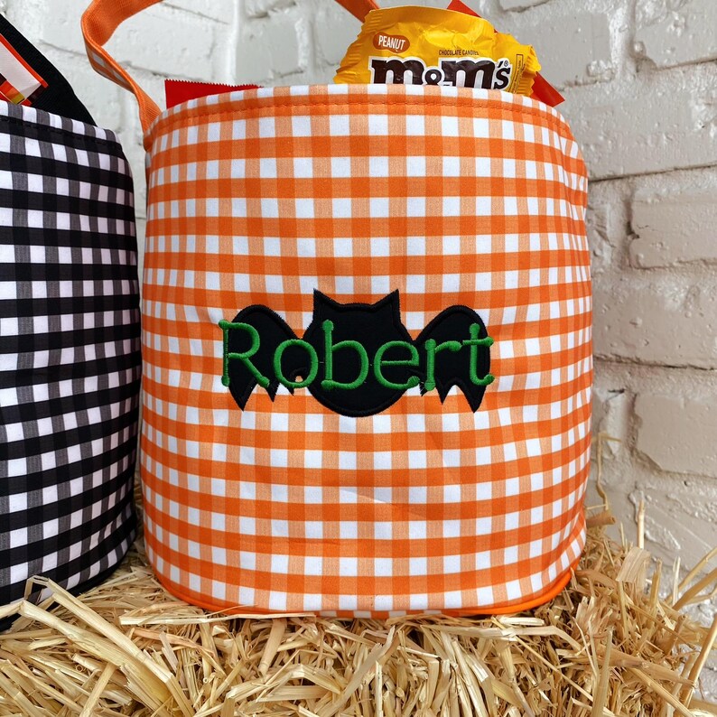 May include: Orange and white gingham fabric trick-or-treat bucket with a black bat and the name "Robert" embroidered on the front.