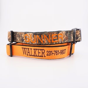 Könnte beinhalten: Zwei Haustierhalsbänder mit schwarzer Hardware. Das obere Halsband hat ein braun-grünes Tarnmuster mit dem in Orange gestickten Namen GUNNER. Das untere Halsband ist leuchtend orange mit braun gesticktem WALKER und 231-761-9807.