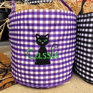 May include: Purple and white gingham trick or treat bucket with a black cat and the name "Cassie" embroidered in green.