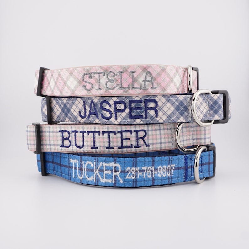 May include: A stack of four fabric dog collars featuring plaid patterns in pink, blue, and white. Each collar is embroidered with a name, including STELLA, JASPER, and BUTTER, while the bottom blue collar displays TUCKER and 231-761-9807.