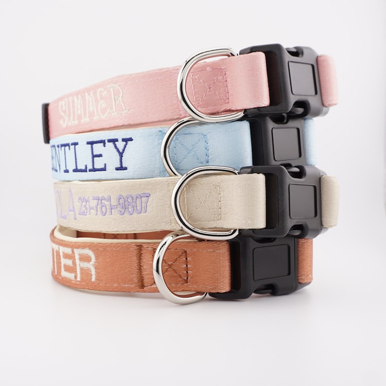 May include: Four dog collars stacked on top of each other. The collars are made of pink, light blue, beige, and orange fabric. Each collar has a black buckle and a silver ring. The collars are embroidered with the names "SUMMER", "BENTLEY", "237-761-9807", and "TER".