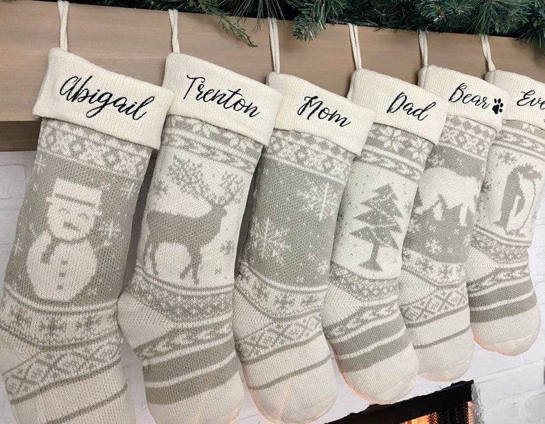 May include: Six white and gray knitted Christmas stockings with personalized names: Abigail, Trenton, Mom, Dad, Bear, and Eve. Each stocking features a different winter-themed design, including a snowman, a deer, snowflakes, a pine tree, a cabin, and a Christmas tree.