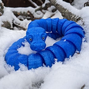 May include: A blue, segmented, snake-like toy with a head resembling a dragon, coiled in a circle on a snowy surface.