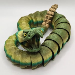 May include: A green and brown segmented snake toy with a yellow eye and an open mouth. The snake is coiled in a circle.