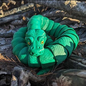 May include: A green segmented snake toy with a detailed head and yellow eyes. The snake is curled up in a circle, with its head in the center.