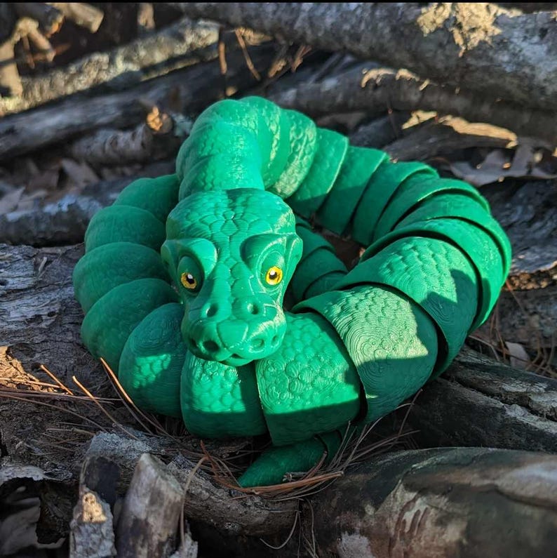 May include: A green segmented snake toy with a detailed head and yellow eyes. The snake is curled up in a circle, with its head in the center.