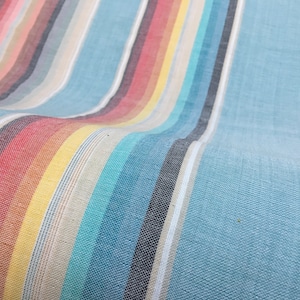 May include: Close-up of a blue and white striped fabric with colorful stripes woven in. The fabric has a soft, textured look.