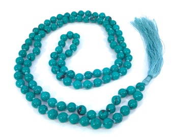 May include: A turquoise blue mala necklace with a tassel. The necklace is made of round beads with black veins.