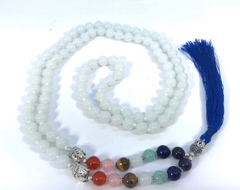 May include: White beaded mala necklace with a blue tassel and seven chakra stones. The stones are red, pink, brown, white, green, blue, and purple.