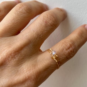 May include: A gold chain ring with a small, clear gemstone.