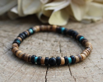 Pode incluir: Um bracelete de contas de madeira com contas pretas e turquesa. O bracelete tem uma única conta preta maior no centro.