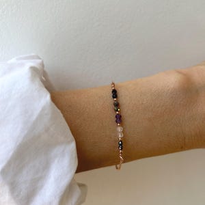 Könnte beinhalten: Ein zartes Armband mit einer dünnen Roségoldkette, die mit einer kleinen Auswahl an facettierten, bunten Edelsteinperlen in Dunkelblau, Violett und Transparent besetzt ist und mit einem einfachen Verschluss aus Roségold schließt.