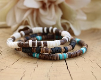 Pode incluir: Uma pilha de três pulseiras feitas de pequenas contas circulares e planas. As contas são em tons de castanho, branco, preto e turquesa. As pulseiras apresentam uma mistura de superfícies de contas lisas, texturizadas e porosas.
