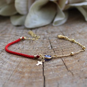 May include: Red string bracelet with a gold chain, a small gold cross charm, and a blue evil eye charm.