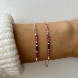 Könnte beinhalten: Zwei zarte Armbänder mit einem Farbverlauf aus rosa und violetten Perlen. Ein Armband hat eine silberne Kette und das andere eine goldene Kette.