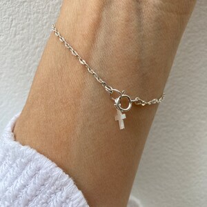 May include: A silver chain bracelet with a small silver cross charm.
