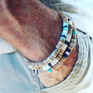 Könnte beinhalten: Drei übereinanderliegende Armbänder aus Holzperlen mit weißen, schwarzen und türkisfarbenen Akzenten.