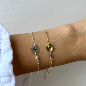 Peut inclure: Deux bracelets délicats, un argenté et un doré, sont présentés. Le bracelet argenté comporte un charm circulaire avec la lettre "J" et une petite perle. Le bracelet doré a un charm avec la lettre "E" et une petite pierre violette.