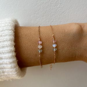 May include: Two delicate gold chain bracelets with three small gemstone beads each. The beads are pink, white, and gray.