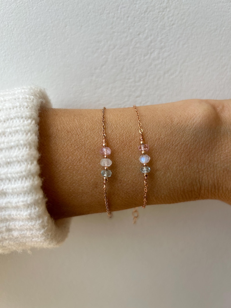 May include: Two delicate gold chain bracelets with three small gemstone beads each. The beads are pink, white, and gray.