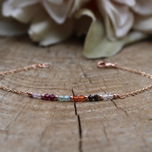 Peut inclure: Un bracelet délicat en chaîne dorée rose avec une rangée de perles de pierres précieuses colorées. Les perles sont dans des tons de rose, rouge, vert, orange, marron et blanc.