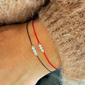 Peut inclure: Deux bracelets avec de petites perles blanches sur un cordon noir et rouge.