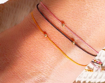 May include: Three bracelets with gold beads on a person's wrist. The bracelets are pink, black, and yellow.