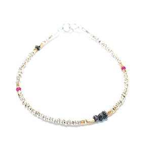 May include: A silver bracelet with small beads, gold accents, and pink and black gemstones.