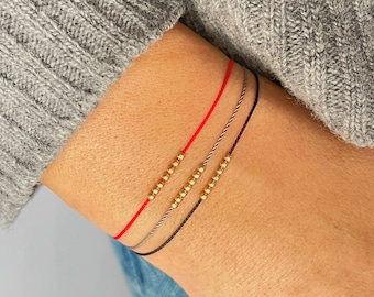 May include: Three bracelets with gold beads on red, gray, and black string.